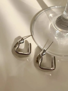 Close-up of modern silver irregular twisted geometric hoop earrings with polished finish