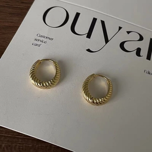 Macro view of gold-plated twisted hoop earrings with ribbed texture on white card