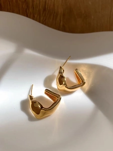 Close-up of gold irregular geometric earrings on a white ceramic plate with high polish