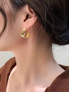 Close-up of golden irregular geometric hoop earrings on a model showing polished finish