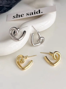Macro detail of glossy gold and silver spiral heart earrings on minimalist ceramic surface