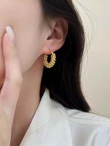 Detailed view of gold hoop earrings with a textured granular finish on a female model