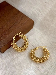Close-up of golden beaded hoop earrings with intricate woven texture on linen background
