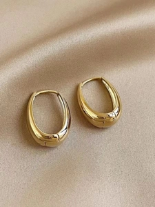 Macro shot of polished gold U-shaped hoop earrings on elegant champagne silk fabric