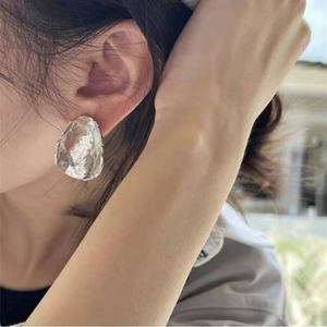 Close-up of irregular textured metal hoop earrings worn by a model in outdoor lighting