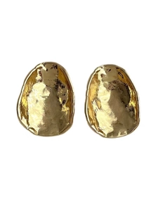 Macro shot of irregular hammered texture on oval golden metal earrings with reflective finish