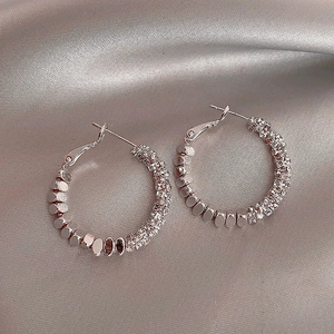 Boucles d'oreilles créoles argentées avec strass pavés sur fond de soie grise