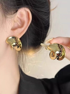 Macro detail of artistic irregular gold twisted metal earrings with a glossy mirror finish