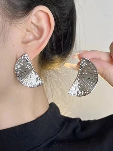 Detail of silver fan-shaped earrings showing pleated metallic texture and modern finish