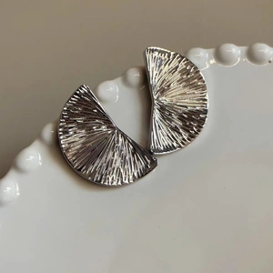 Polished silver fan-shaped earrings with radial pleat texture on white wavy ceramic plate