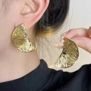 Golden fan-shaped textured metal earrings with radial pleats on an elegant female model