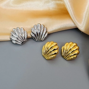 Detailed view of gold and silver shell earrings with polished texture on silk background