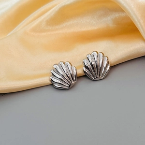 Macro view of silver seashell stud earrings with textured ridges and micro-inlaid zircon