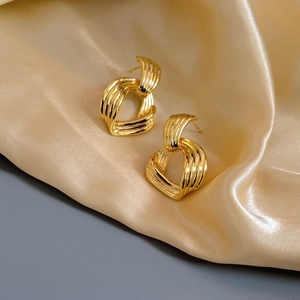 Gros plan de boucles d'oreilles dorées torsadées à rayures sur tissu en soie