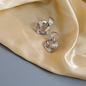 Détail macro de boucles d'oreilles argentées au design torsadé sur tissu en soie dorée