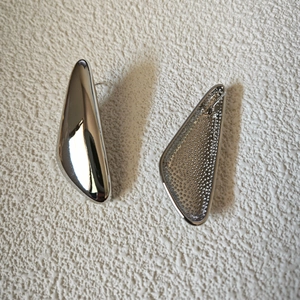 Macro detail of irregular silver geometric earrings showing mirror finish and honeycomb texture