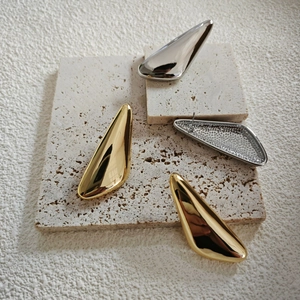 Detailed view of teardrop gold and silver geometric earrings on travertine stone