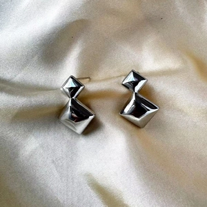 Gros plan de boucles d'oreilles losanges doubles en argent sur tissu en satin jaune