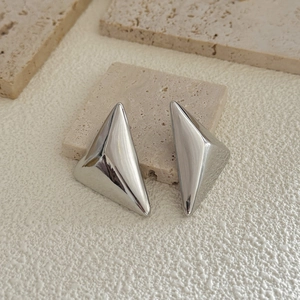 Detail of silver geometric 3D triangle earrings on a natural travertine stone stand