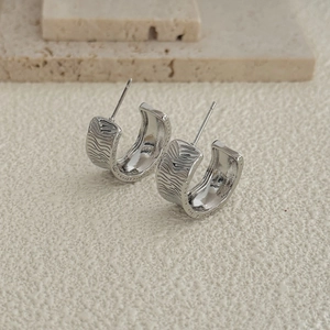 Detail of silver C-shaped earrings with unique water ripple texture on stone background