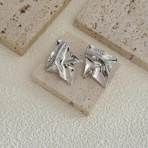 Irregular silver geometric earrings with a polished liquid metal finish on stone background