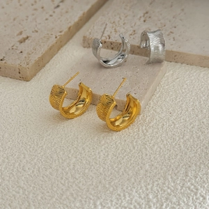 Macro detail of C-shaped metal earrings with textured gold and silver wavy finish