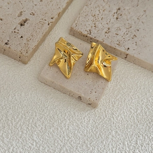 Macro shot of irregular folded gold geometric earrings with a high-polished metallic finish