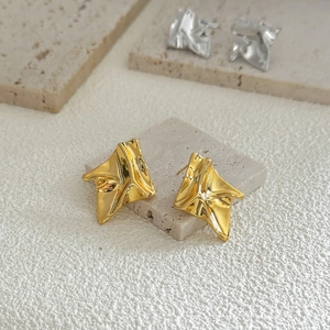 Macro detail of irregular pleated geometric metal stud earrings on stone display