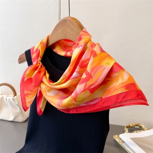 Detail of vibrant floral satin scarf draped over a black top on a wooden hanger