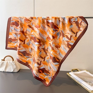 Artistic printed silk scarf draped on a metal stand with a white fashion handbag