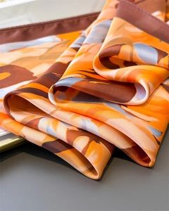 Close-up of printed silk scarf showing vibrant orange floral pattern and soft satin texture