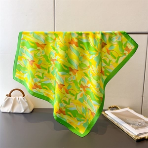 Close-up of elegant floral silk scarf with green borders hanging on a metal rack
