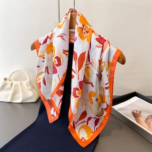 Foulard en soie aux motifs floraux orange et rouge suspendu sur un cintre en bois
