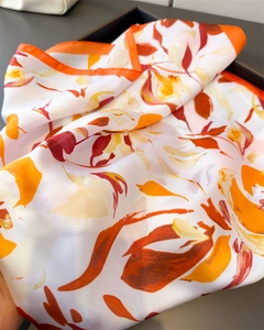 Détail du foulard floral en satin avec bordure orange sur un plateau sombre élégant