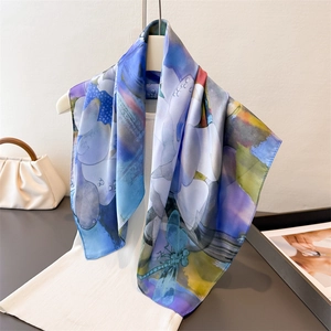 Detail of silk-like scarf with dragonfly floral print draped on a hanger and clothing