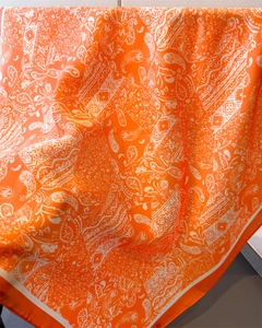 Détail de l'écharpe carrée en soie orange montrant le motif paisley et le drapé lisse