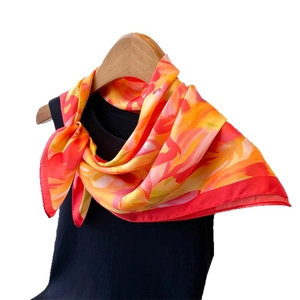 Vibrant floral silk-like square scarf tied on a black knit top with a wooden hanger
