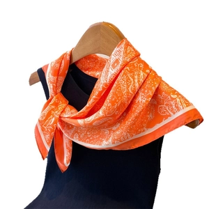Élégant foulard en soie orange avec motif paisley affiché sur un vêtement bleu