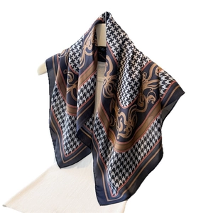 Classic houndstooth and golden baroque print silk-like scarf draped on a wooden hanger