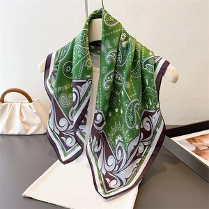 Elegant green paisley silk scarf with contrast borders hanging on a minimal hanger