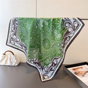 Macro detail of a green paisley silk scarf draped elegantly with a white fashion handbag