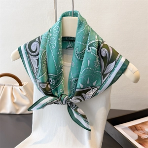 Detail of green paisley print silk scarf knotted on a white sleeveless garment
