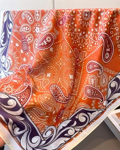 Macro shot of orange paisley silk scarf showing elegant folds and smooth fabric texture