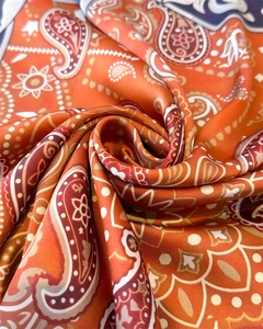 Macro shot of orange paisley silk square scarf showing detailed patterns and satin texture