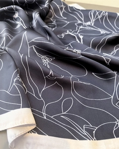 Close-up of elegant black silk scarf featuring delicate white floral line art patterns
