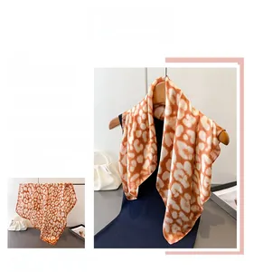 Detail of elegant leopard print silk scarf with warm orange and beige tones on a hanger