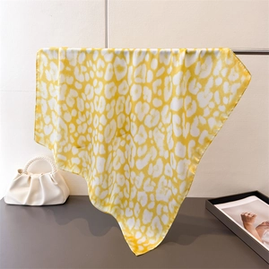 Elegant yellow leopard print silk square scarf with satin finish draped on a display rack
