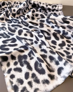 Detailed close-up of luxurious silk satin fabric with black and white leopard print and fine edges