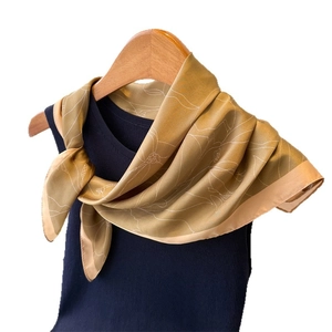 Elegant gold silk scarf with white floral prints displayed on a blue knit top