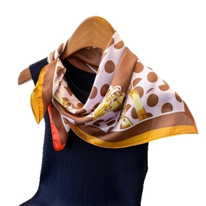 Silk-like square scarf with brown polka dots and gold chain print hanging on a hanger